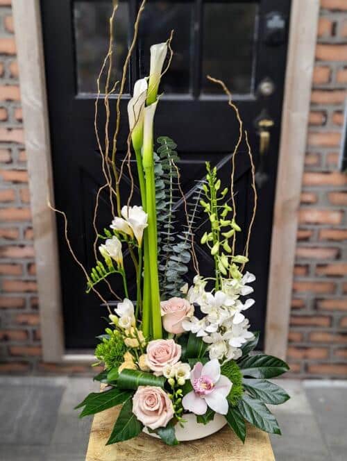 a large asymmetrical european arrangement featuring large white calla llilies, blush roses, white orchid blooms and more.