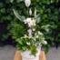 A Garden of Peace sympathy arrangement with a peace lily, orchid, parlour palm, tropical greenery, and an angel figurine in a white ceramic pot