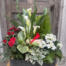 A planted sympathy basket of white calla lilies, red roses, white kalanchoe and mixed green foliage in a woven planter, accented with a small red cardinal.
