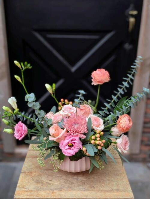 Front view of a delicate blush floral arrangement in a pale pink ribbed ceramic bowl featuring roses, lisianthus, chrysanthemum, hypericum berries, and eucalyptus, from The Watering Can Flower Market.