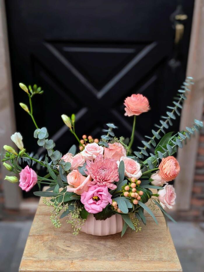 Front view of a delicate blush floral arrangement in a pale pink ribbed ceramic bowl featuring roses, lisianthus, chrysanthemum, hypericum berries, and eucalyptus, from The Watering Can Flower Market.