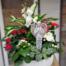 A lush sympathy arrangement in a round white stone bowl featuring white orchids, red roses, an angel figurine, and mixed tropical foliage at The Watering Can.