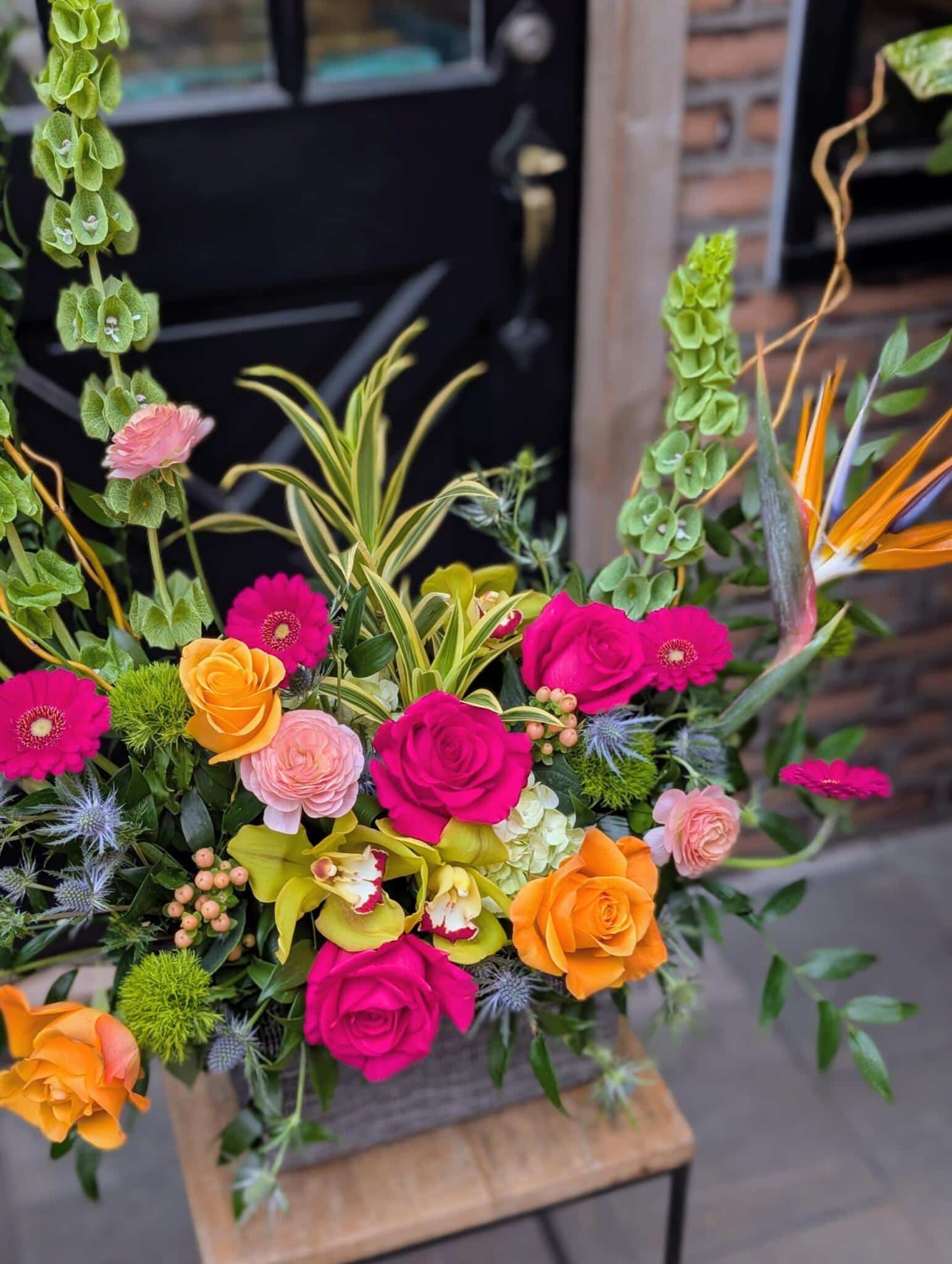 A tall modern floral arrangement called Citrus Splash featuring upright orange and pink blooms with long stems in a dark container.