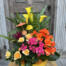 A bright planted arrangement in a yellow ceramic bowl with yellow calla lilies, orange begonias, pink kalanchoe and peach roses, topped with a tiny cocktail umbrella.